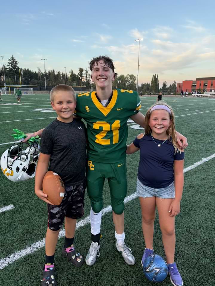 Three children, a boy and two girls, pose happily on a football field